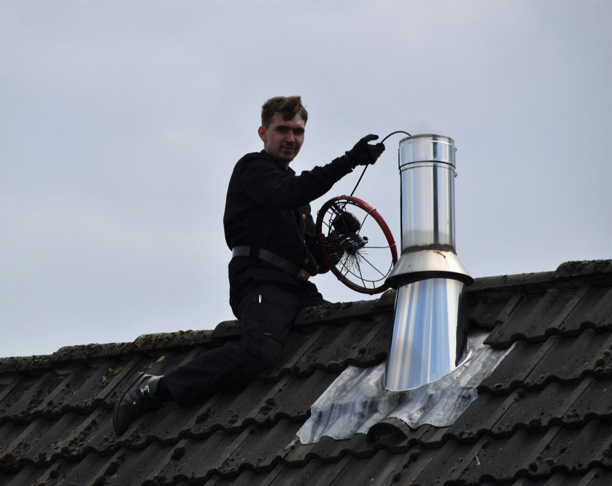 Schornsteinfeger reinigt einen Edelstahlschornstein auf einem Ziegeldach, Symbolbild