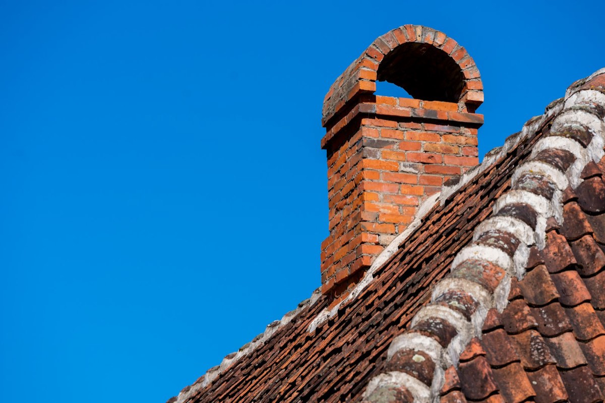 Gemauerter Schornstein auf einem Ziegeldach vor blauem Himmel